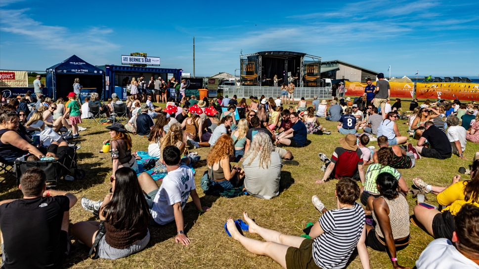 Sluagh nan suidhe air an fheur aig Fèis Chiùil Thiriodh air là ghrianach