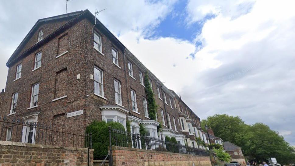 Terrace of tall Georgian properties beside a river all with large white framed windows