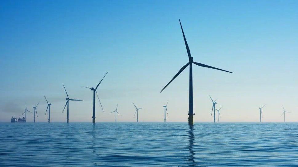 A number of wind-turbines emerging from the ocean surface against a blue sky