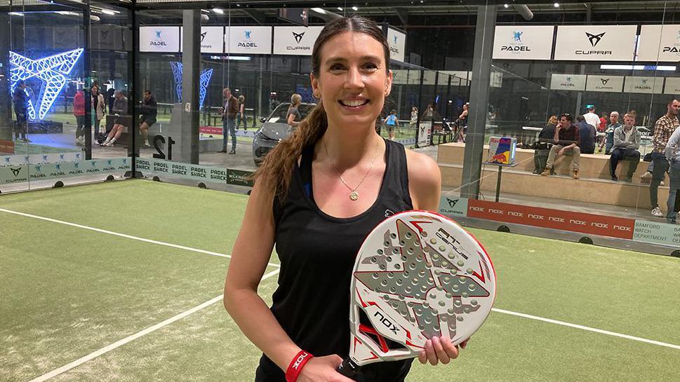 A woman smiling standing on a court holding a perforated padel raquet