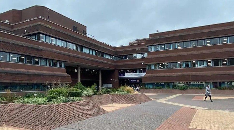 A red-brick brutalist office block, surrounded by brick-built raised flower beds which are surrounded by brick paving.