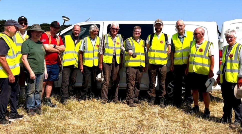 Twelve members of the Norton Disney History and Archaeology Group posing for the camera in a field in front of a white van in high-vis vests