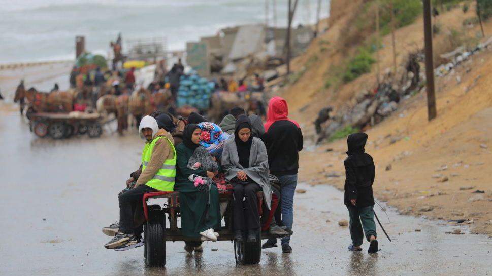 Male and female Palestinians sitting on a trailer in rainy weather