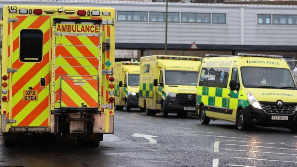 Ambulances lined up outside a hospital. Three are facing toward the camera, one has its back to the camera. They have florescent livery.