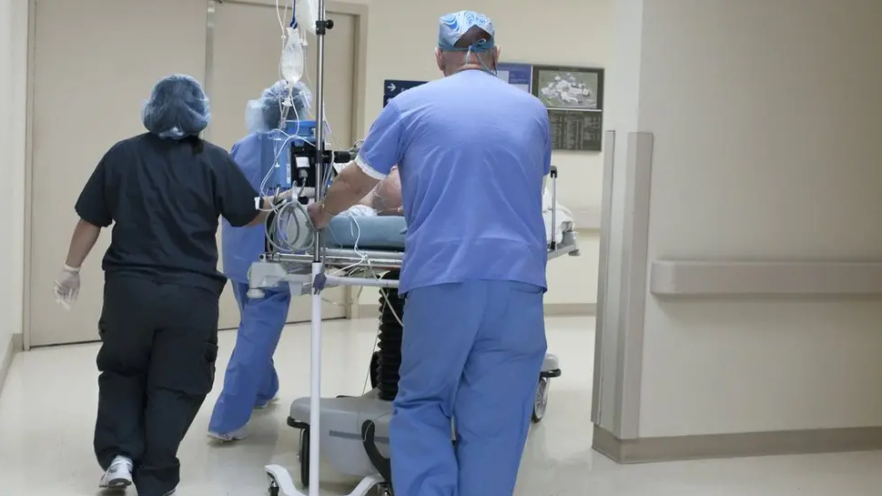 Three members of NHS staff push a patient in a hospital bed along a corridor