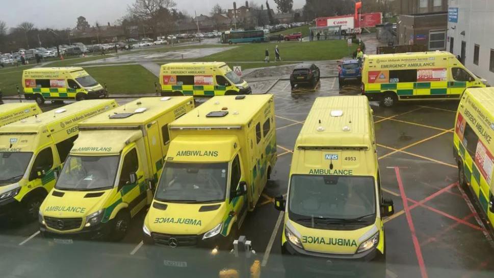 Several ambulances outside hospital. The ambulances are yellow in colour with green stencils saying "ambulance" parked on a hospital campus.