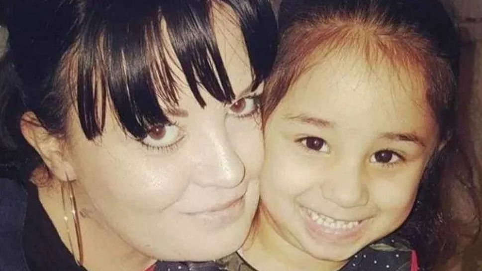 A woman with black hair and a child with brown hair smile at the camera with their cheeks pressed together