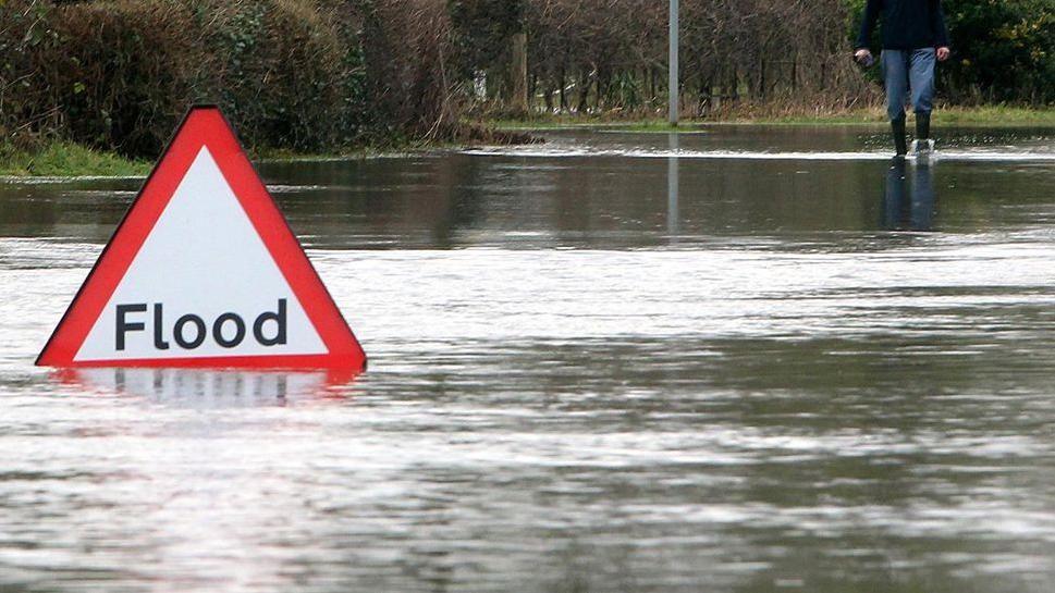 A flood sign, partly submerged in water on a flooded road