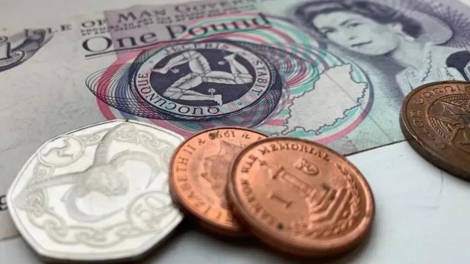 A close-up of Manx money, including a £1 note, with a 50p coin and three 1p coins on top.