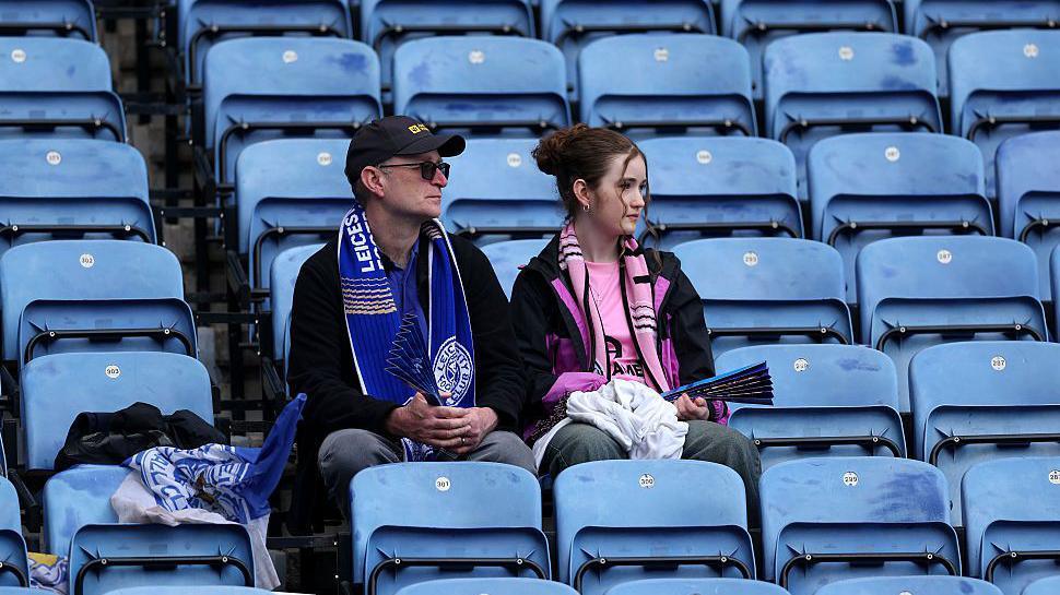 Two Leicester City fans sit among empty blue seats