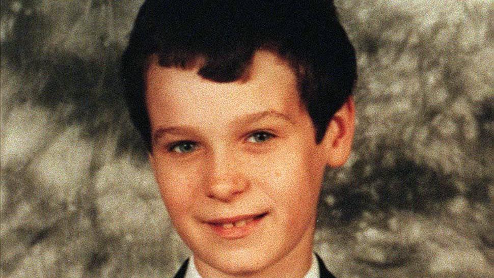 Headshot of a boy smiling at camera, standing in front of a grey background