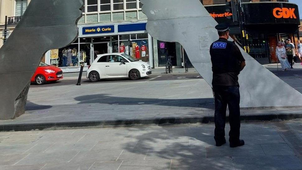 A police officer standing on a high street with their back to the camera