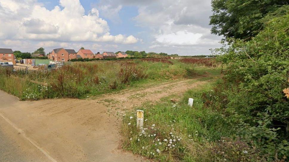 The site of 35 proposed houses on Station Road, Digby. There is a farm track leading into a field in the foreground, and behind the field are new-build houses and construction items.