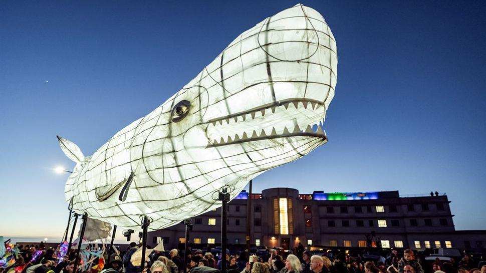 The giant white, illuminated, tissue-covered wicker whale is "walked" down Morecambe promenade at dusk during February's Baylight Festival.