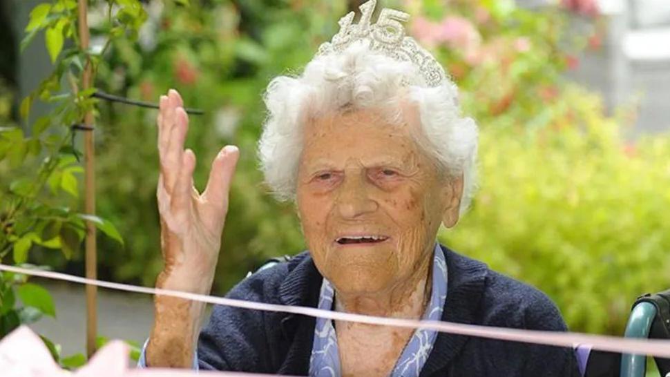 An elderly women waving while wearing a crown with the numbers 115 on it