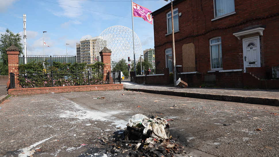 Pile of burnt out rubbish on street in Belfast's Village area with UVF flag flying in the background