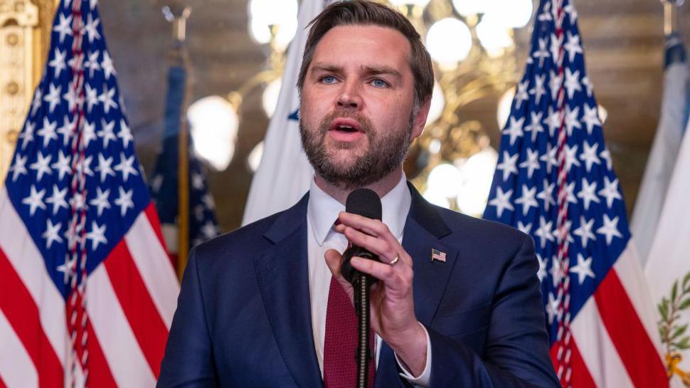 US Vice President JD Vance standing in front of two American flags