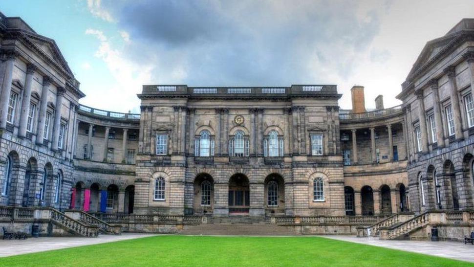 Old Edinburgh University stone building featuring lots of columns and windows and a green lawn in front 