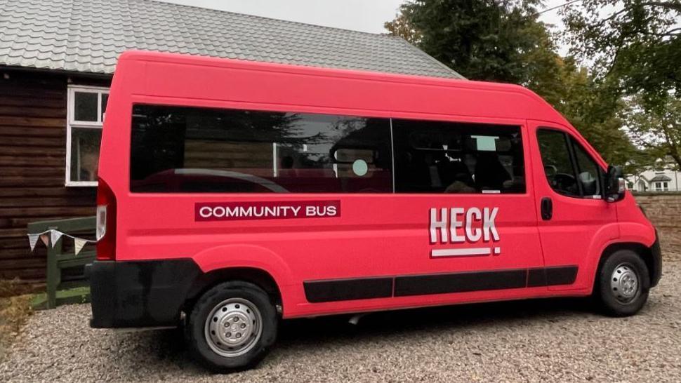 A pink minibus with the words "community bus" and "Heck" written on the side.