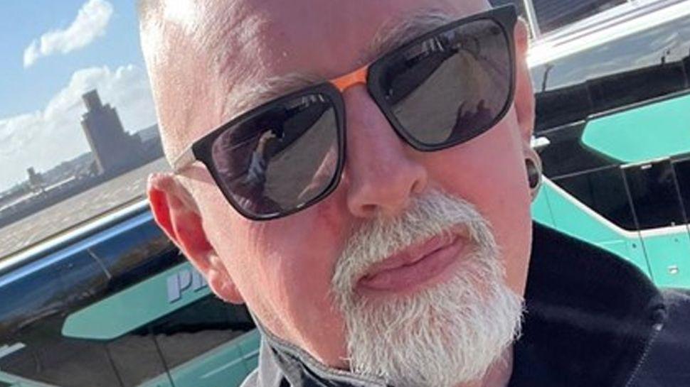 Close up of Stuart Burns. He is standing outside in the sunshine and is wearing sunglasses. He has a white goatee and a shaved head.