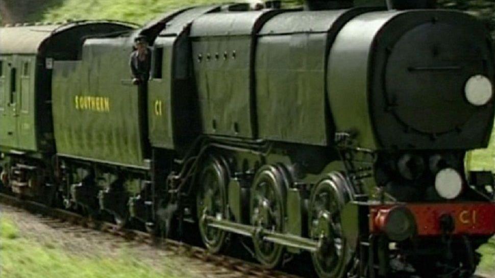 Bulleid's Q1. It is dark green with a red bumper and is pictured on a rail track.