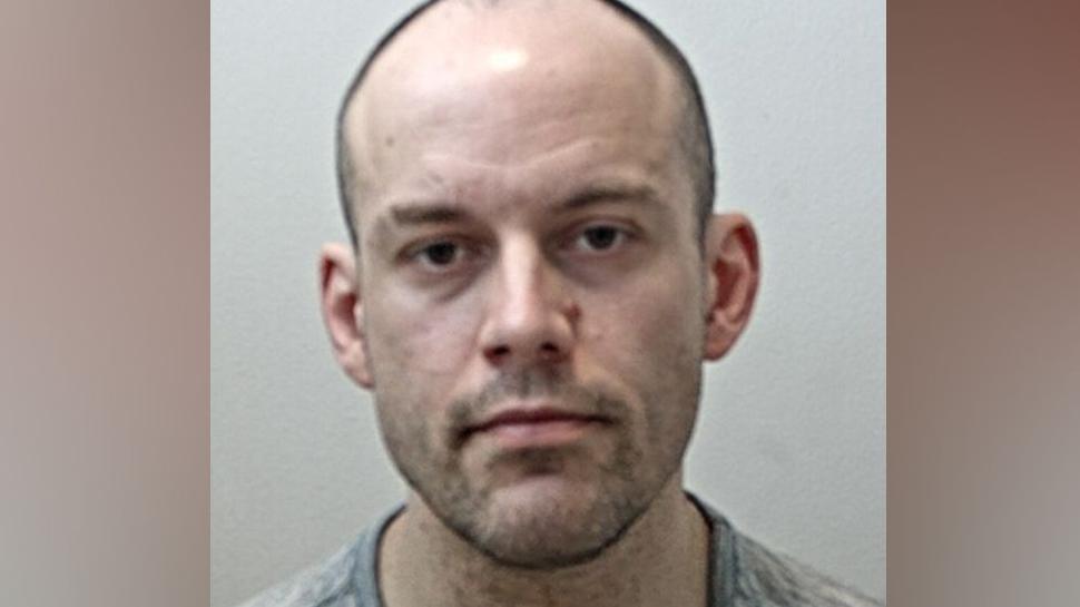 Matthew Matthiason's mugshot. He is balding with very short dark hair and stubble