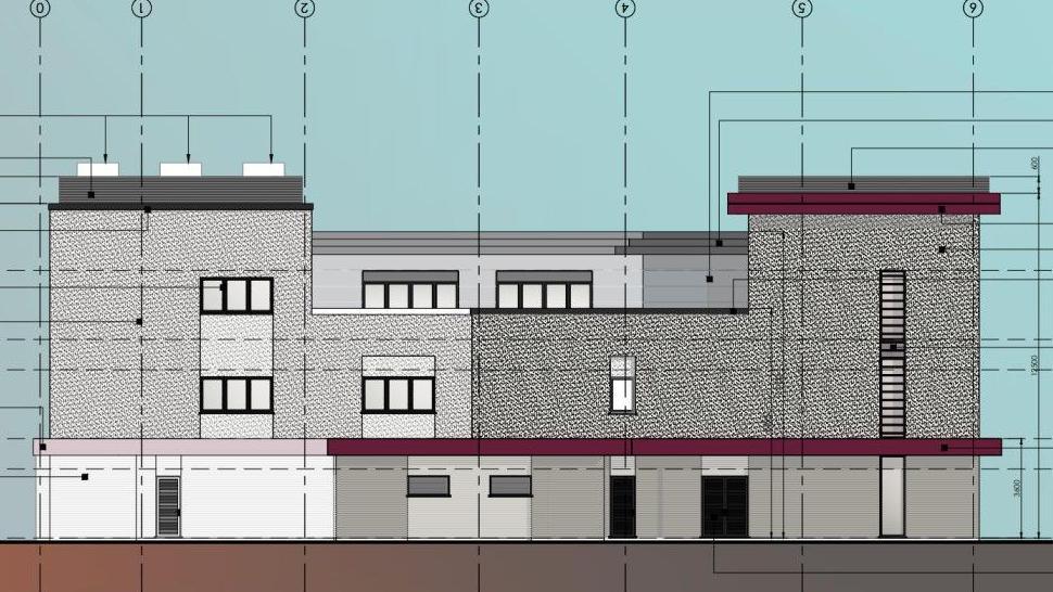 An architectural drawing of the proposed fire station which spreads across three floors. Its facade has a mostly grey and charcoal exterior, with some maroon colouring on the lower floor and one side of the building's roof.