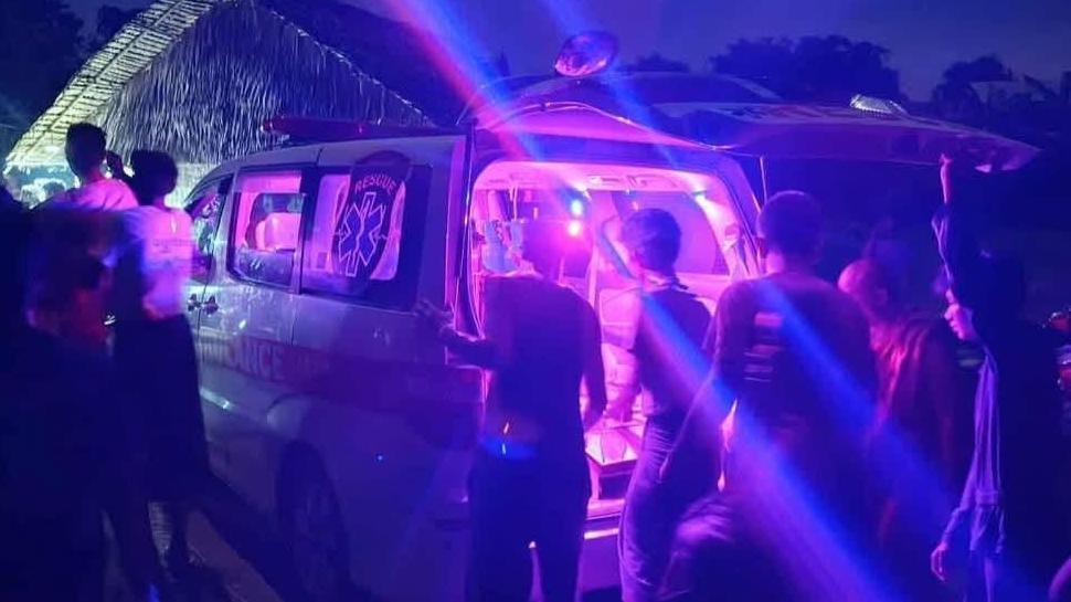 Një ambulancë mund të shihet, me drita vjollcë që shkëlqejnë fort brenda, me një grup njerëzish të mbledhur përreth
