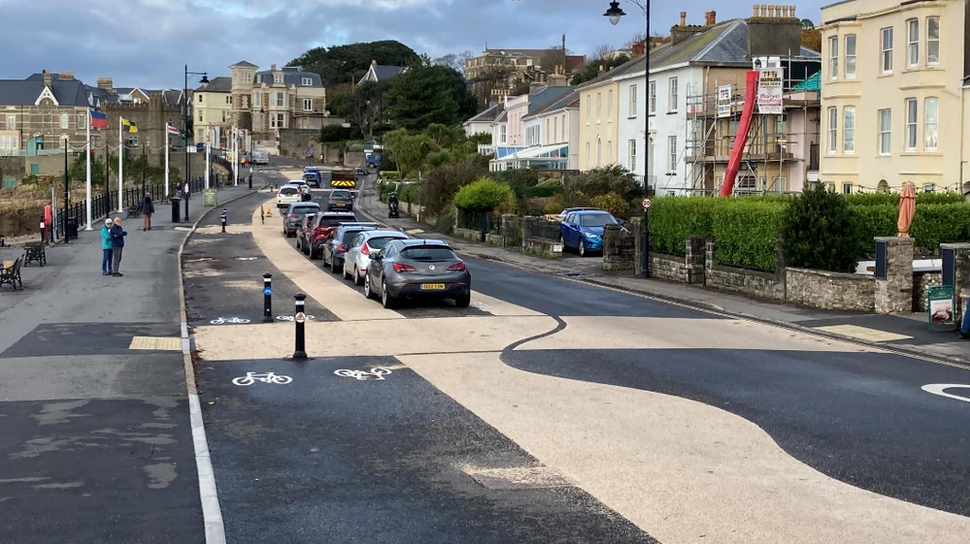 A view of Clevedon seafront. The wavy road markings, stretches of beige tarmac and a double cycle lane on the left-hand side. A row of Victorian houses stands to the right of the picture.