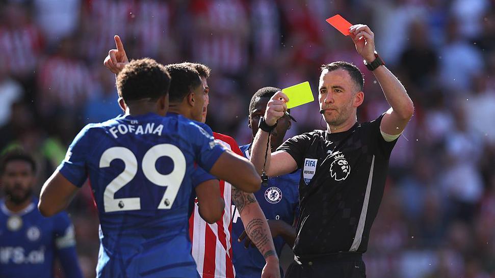 A Chelsea player is sent off by a referee who brandishes a red card