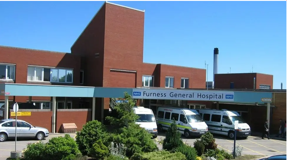 Furness General Hospital is a red brick building with blue and white signs that read: "NHS Furness General Hospital". Ambulances are parked out front.