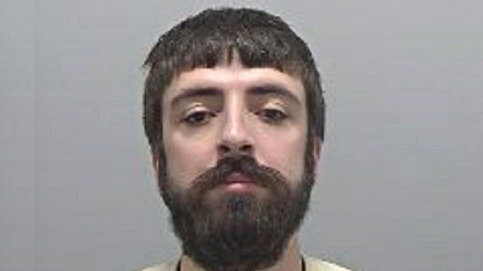 A police custody image of Kyle Clifford, who has a thick dark beard and is standing against a grey backdrop

