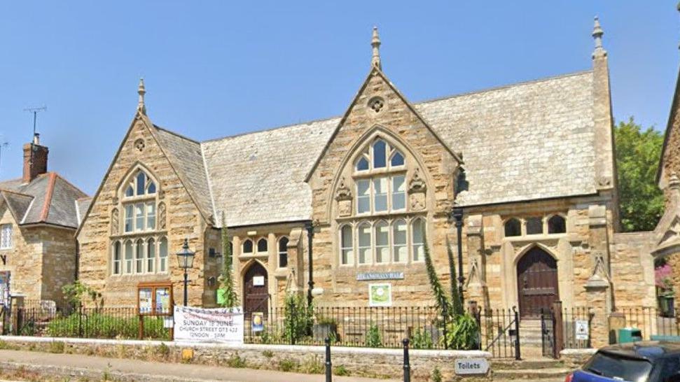 A former village school building, built from stone in the late 19th century, with ornate arched windows and a high pitched roof