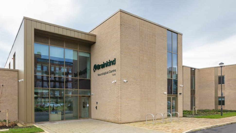 The outside of the Brainkind Neurological Centre building, with light brown pavements and light brown bricks and a large window at the front