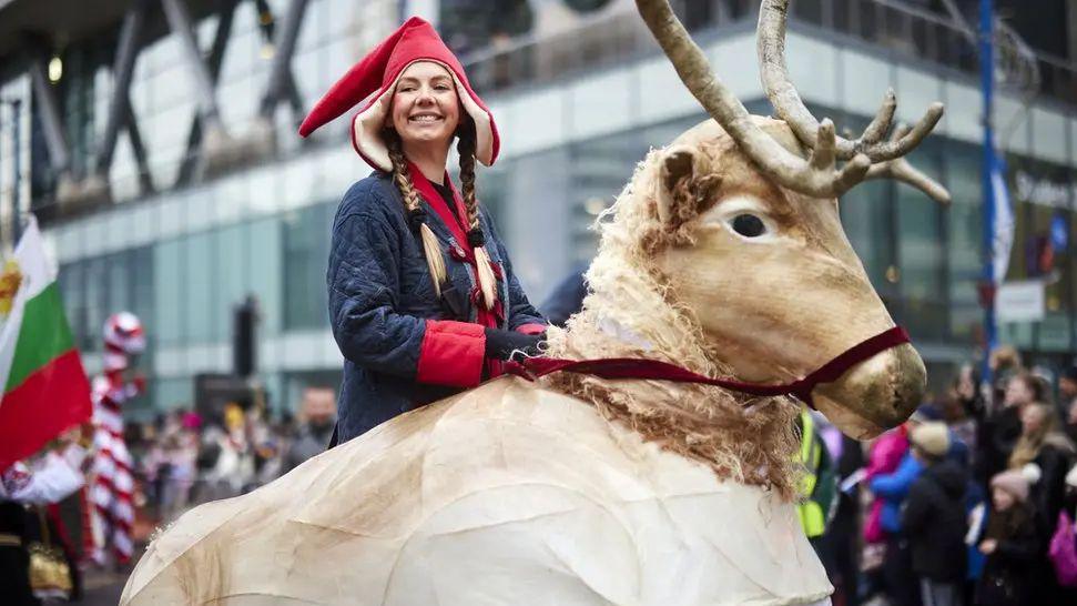 A woman wearing a red hat riding a reindeer puppet in Manchester city centre