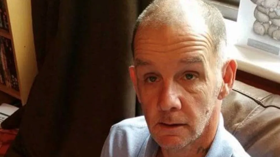 Phillip Breach, a man with shaven, greying hair and a light blue shirt sitting on a brown sofa 