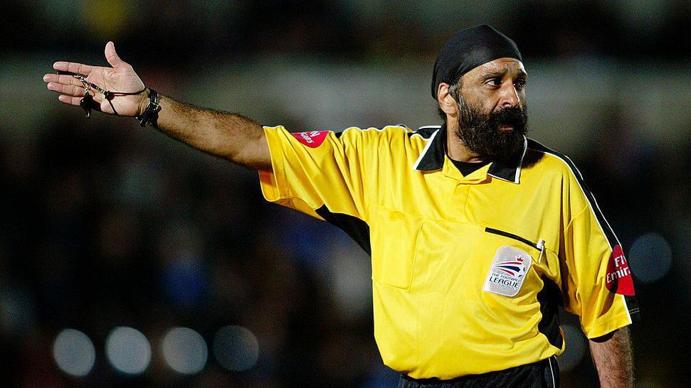 Jarnail Singh raises his arm indicating play on while refereeing an EFL match.