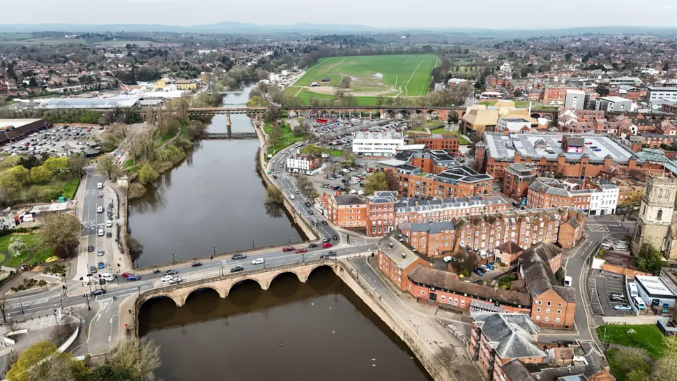 An aerial shot of Worcester, showing Worcester Bridge crossing the River Severn and buildings and roads on either side of the water.