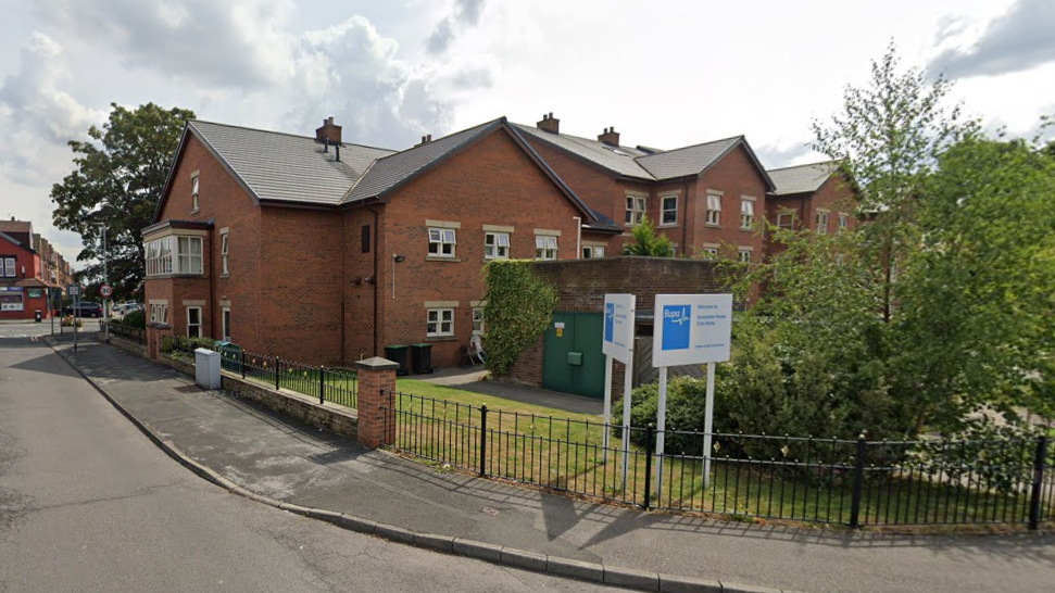 Exterior view of Sunnyview House care home. It is a brick building which looks like a house. There is a white sign outside with Bupa's blue logo on it.