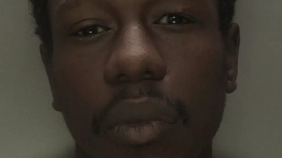 A police mugshot of a man staring at the camera in front of a grey background