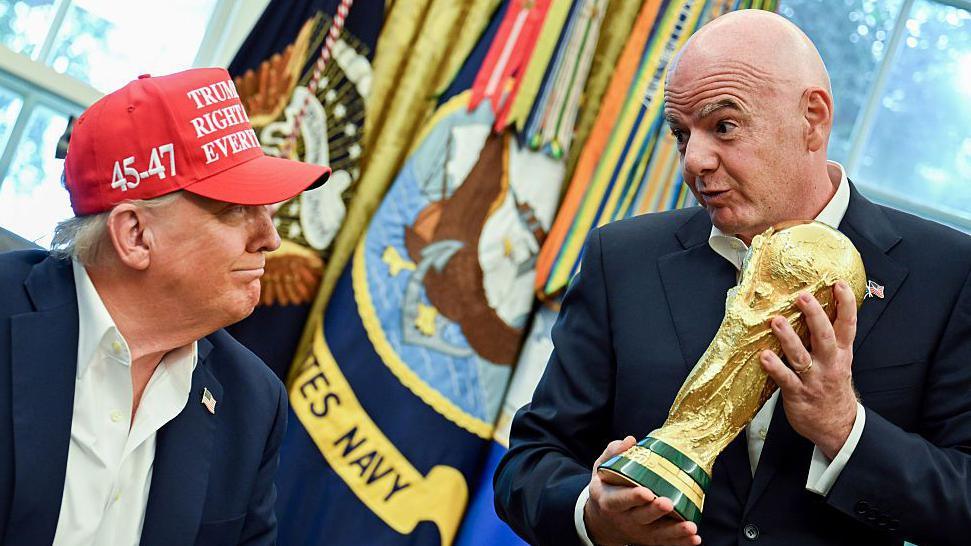 Gianni Infantino holding the World Cup in the Oval Office next to Donald Trump