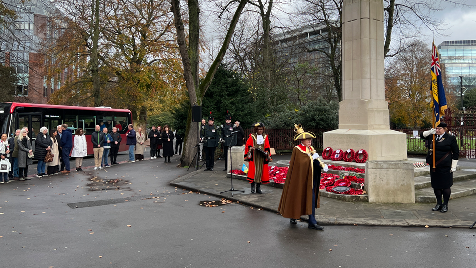 Armistice Day ceremony in Reading with a small group of people watching alongside the war memorial with wreaths of poppies laid on its steps