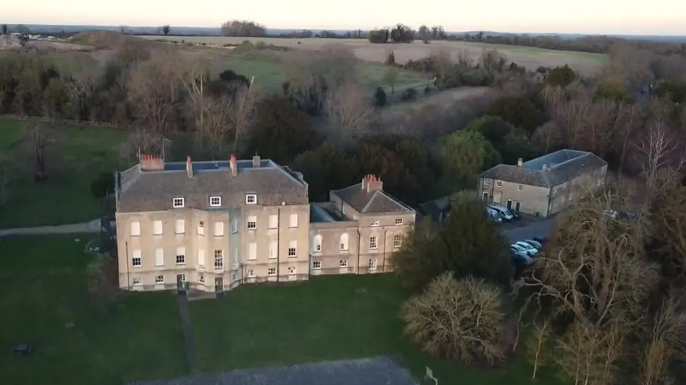 A bird's eye view of Woodeaton Manor School, which looks like a mansion or stately home, with another building to the right of it. There are fields and trees surrounding it 