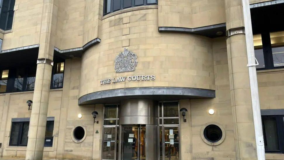 The exterior of the Bradford Crown Court building, with light coloured stone and silver letters of "The Law Courts" written on the front.