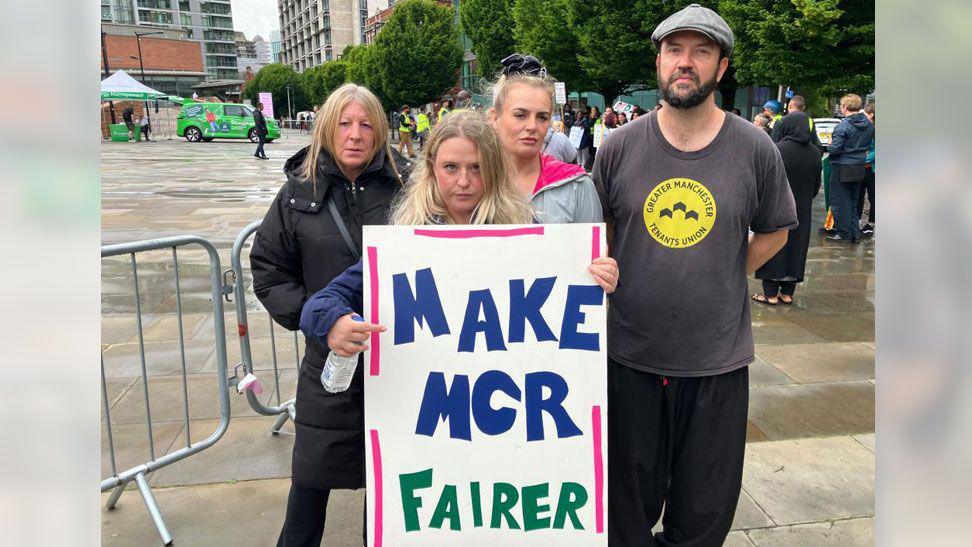 A group of three women and one man are protesting outside Manchester Central. A woman at the front of the group is holding a banner which says "make MCR fairer".