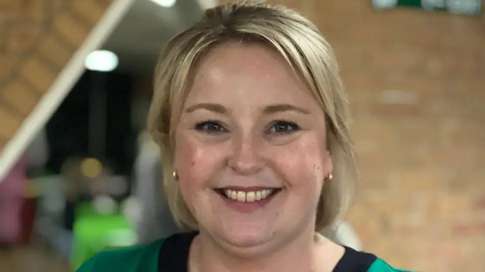 A woman with should-length blonde hair. She is smiling at the camera