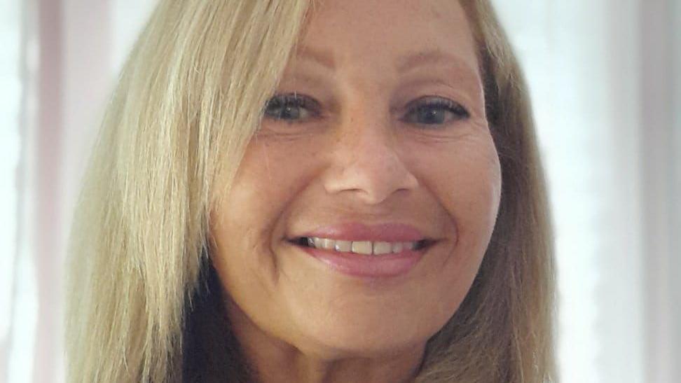 Head shot photograph of a woman with a blonde shoulder length hair, smiling at the camera