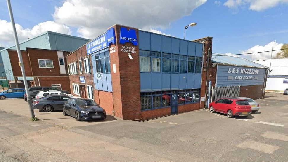 Various buildings are in the background, in this generic image of buildings. Vehicles are parked in front of some of the buildings.