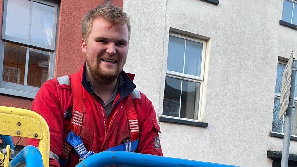 Kit Hughes stands smiling after bringing down the cat from the roof. He is standing on an access platform with blue rails.