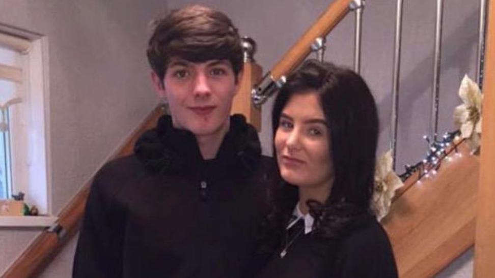 Kasey Anderson has short brown hair and is wearing a black hoodie. He is stood with Molly Anderson who had black hair and is wearing a black top with a white shirt and silver pendant necklace. 